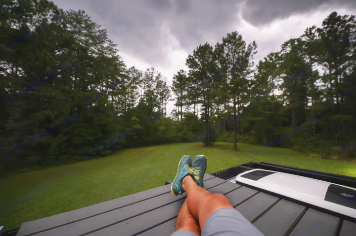Relaxing on an RV rental with legs propped up, overlooking a forest under cloudy skies. Perfect outdoor retreat.. Ford Transit 250 2023