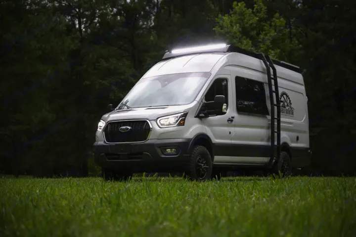 White Ford Transit camper van with bright roof lights & off-road tires, parked on grass. Ideal for your next rv rental adventure.. Ford Transit 250 2023