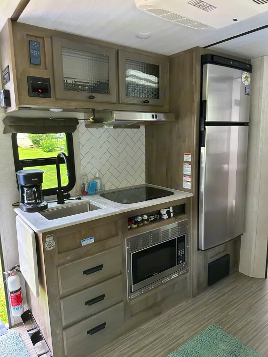 Modern RV rental kitchen featuring a fridge, microwave, sink, and cooktop for comfortable living on the road.. Forest River Surveyor Legend 2021