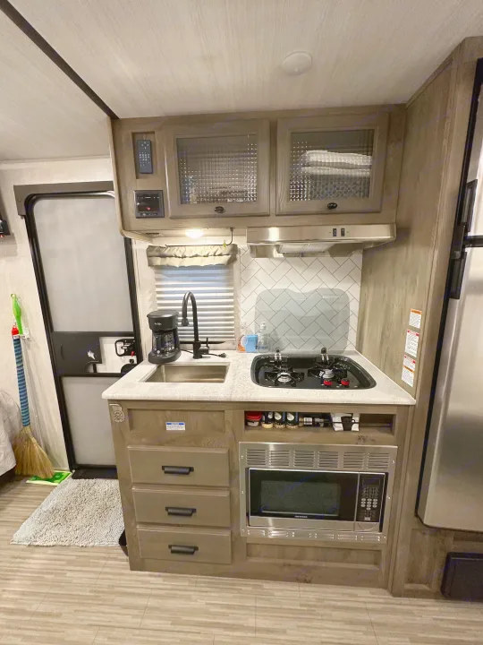 This RV rental features a well-equipped kitchen with a sink, two-burner stovetop, microwave, and overhead storage.. Forest River Surveyor Legend 2021