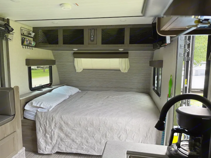 Cozy RV rental bedroom featuring a comfy bed with light gray bedding, overhead storage, and a coffee maker nearby.. Forest River Surveyor Legend 2021