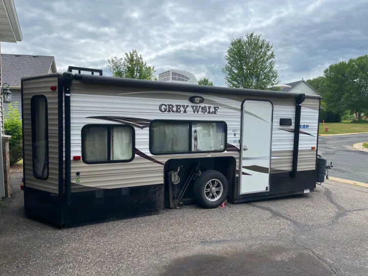 A "Grey Wolf" travel trailer RV rental, with an exposed wheel in its bay, parked on a paved driveway.. Forest River Cherokee Grey Wolf 2015