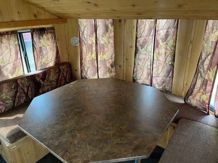 Spacious RV rental interior with wooden walls, camo curtains, large table, and booth seating.. Forest River Cherokee Grey Wolf 2015