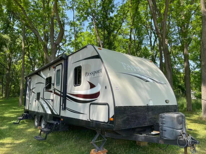 Beige Passport travel trailer, an excellent rv rental option, parked in a sunny, tree-filled natural setting.. Keystone RV Passport Ultra Lite 2015