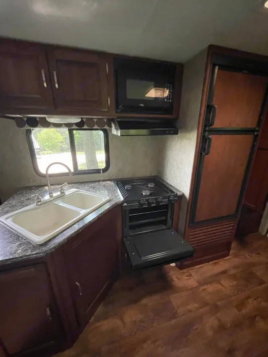 RV rental kitchen featuring a double sink, microwave, range with open oven, and a tall refrigerator.. Keystone RV Passport Ultra Lite 2015
