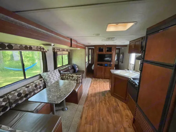 Spacious RV rental interior featuring a comfy dinette, living area with TV, and a functional kitchen. Wood flooring & large windows enhance comfort.. Keystone RV Passport Ultra Lite 2015