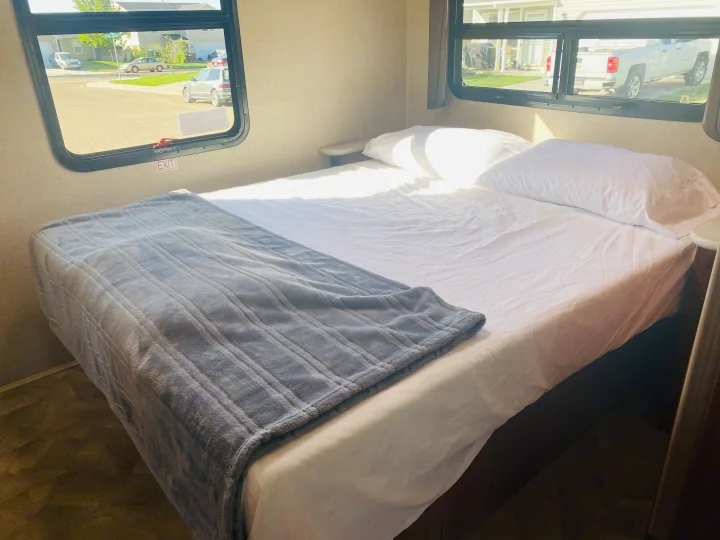Cozy RV rental bedroom with a comfy bed, sunlit windows, and a view of a quiet street. Ideal for travel and adventure.. Jayco Redhawk 2016