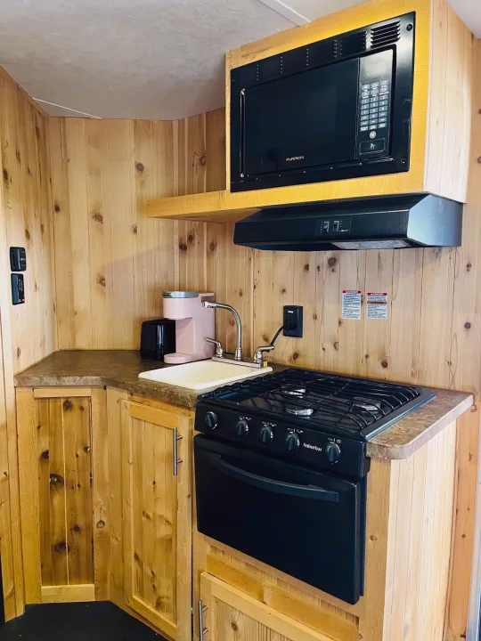 This RV rental kitchen has a microwave, gas stove with oven, sink, and wood cabinetry, perfect for travel.. Forest River Cherokee Grey Wolf 2015