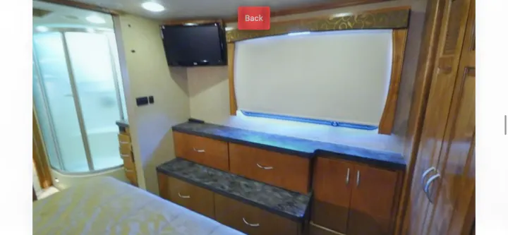 RV rental bedroom with bed, TV, built-in storage, and an enclosed shower. Enjoy modern comforts on the road.. Monaco Vesta 2012