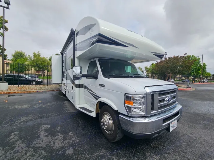 White Class C RV rental motorhome with slide-out, parked on wet asphalt, ready for outdoor travel.. Jayco Greyhawk 2018