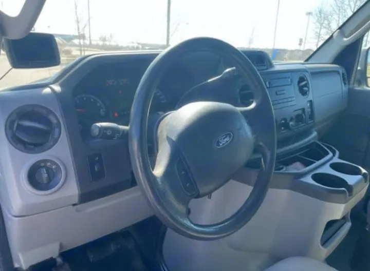 Interior of an RV rental showing the driver's area with a Ford steering wheel, dashboard, and center console with cupholders.. Ford Econoline 2012