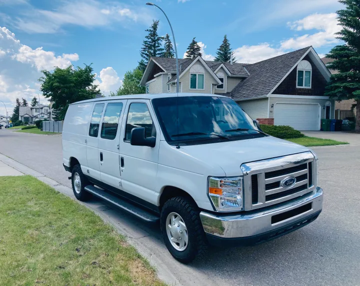 White Ford passenger van parked on a residential street. Consider this spacious vehicle for your next RV rental.. Ford Econoline 2012