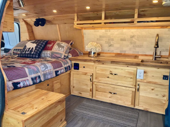 Cozy RV rental interior: wood-paneled camper van bedroom and kitchenette with sink, tiled backsplash, and storage.. Ford Econoline 2012