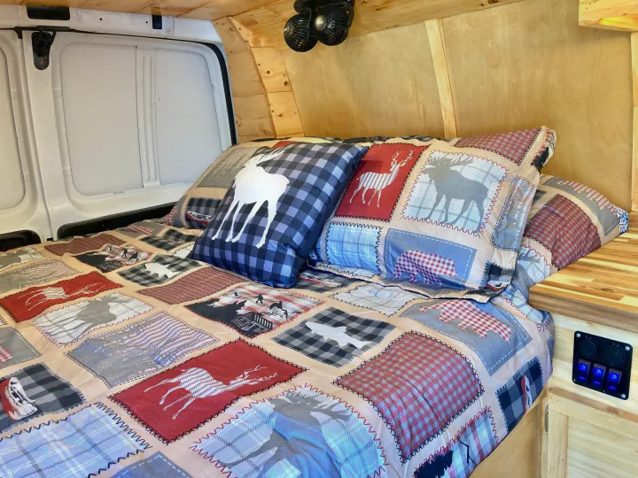Cozy RV rental bed featuring a rustic patchwork comforter with animal motifs, wood-paneled walls, and ceiling fans.. Ford Econoline 2012