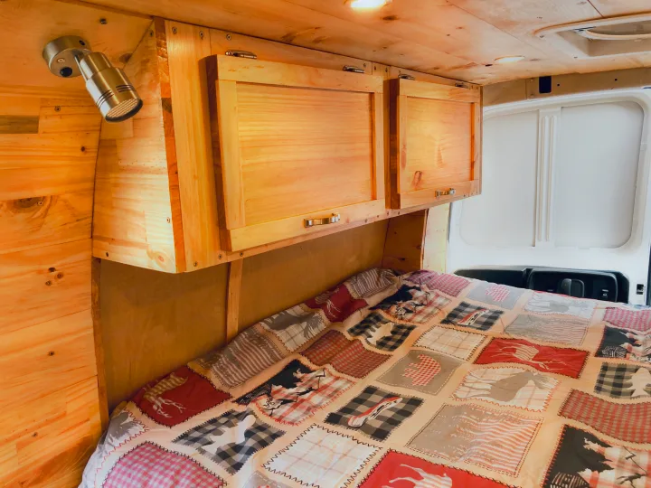 Cozy RV rental interior with light wood paneling, overhead cabinets, and a patterned bed for comfortable travel.. Ford Econoline 2012