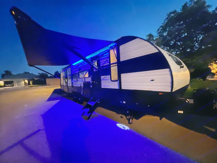Night view of an RV rental: blue LED awning lights illuminate the ground, with a projected logo, creating a vibrant outdoor space.. Forest River Cherokee Grey Wolf 26DBH 2023