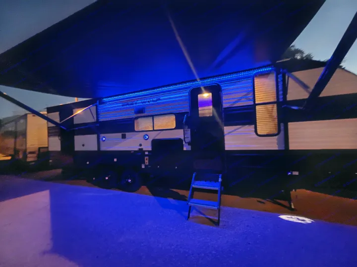 This RV rental is beautifully illuminated at night by blue LED lights, highlighting the travel trailer and awning for a cozy camping setup.. Forest River Cherokee Grey Wolf 26DBH 2023