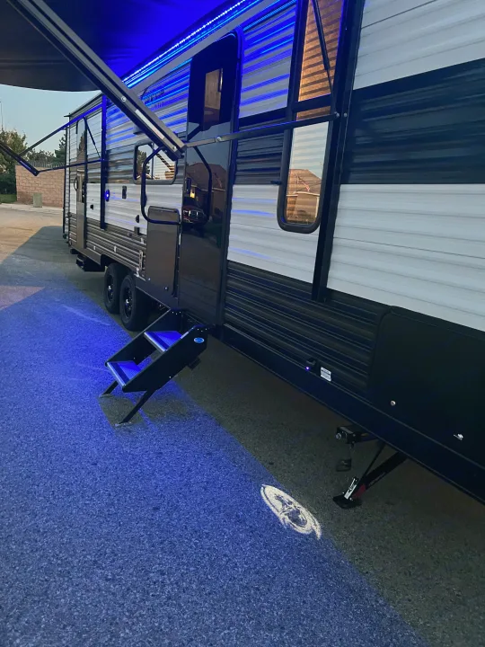 RV rental featuring blue LED awning lights, extended entry steps, and a unique logo projected on the ground for evening ambiance.. Forest River Cherokee Grey Wolf 26DBH 2023