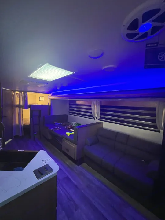 Cozy RV rental interior at night with blue lights, featuring a dinette, sofa, and bed area.. Forest River Cherokee Grey Wolf 26DBH 2023