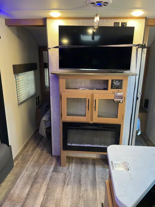 Compact RV rental living space with TV, cabinets, and electric fireplace. Features wood-look flooring and a window.. Forest River Cherokee Grey Wolf 26DBH 2023