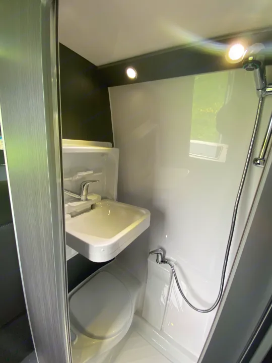 The white interior of this RV rental wet bath includes a compact sink, toilet, and handheld shower.. Mercedes-Benz Sprinter 2012