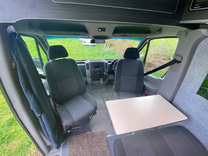 Cozy RV rental camper van interior showing front cab seats & a rear table setup.. Mercedes-Benz Sprinter 2012
