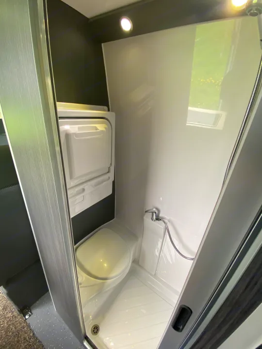 This RV rental boasts a compact, clean bathroom with a toilet, shower, and bright interior lighting.. Mercedes-Benz Sprinter 2012