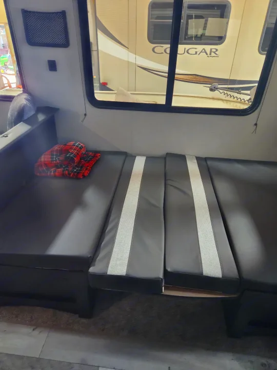 Inside an RV rental: a modern dinette with dark and light gray cushions, plus a window showing the exterior.. Keystone RV Springdale 2022