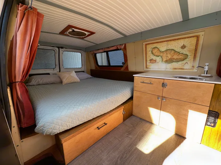 Cozy RV rental interior featuring a comfortable bed, functional kitchen with sink, and smart storage solutions for travel.. Ford E150 2002