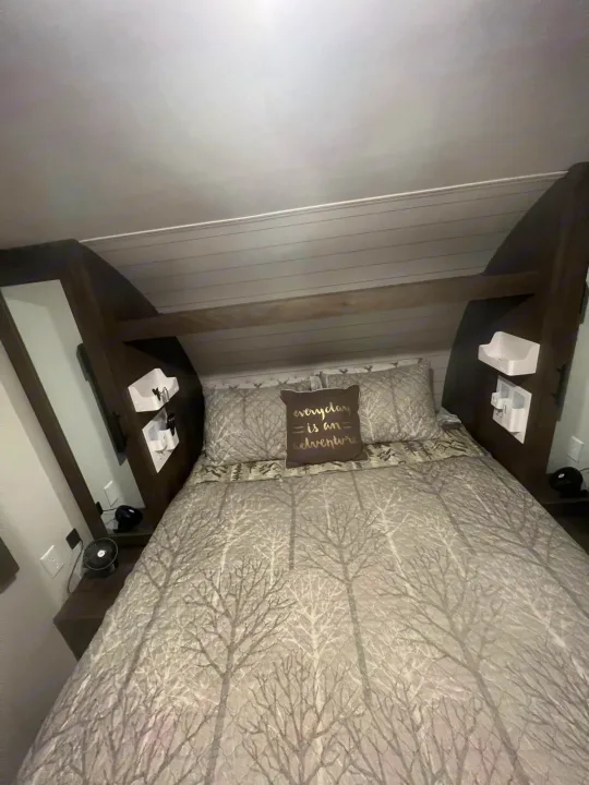 RV rental bedroom featuring a tree-patterned bed, 'everyday is an adventure' pillow, and built-in bedside storage.. Forest River Wildwood X-Lite 2021