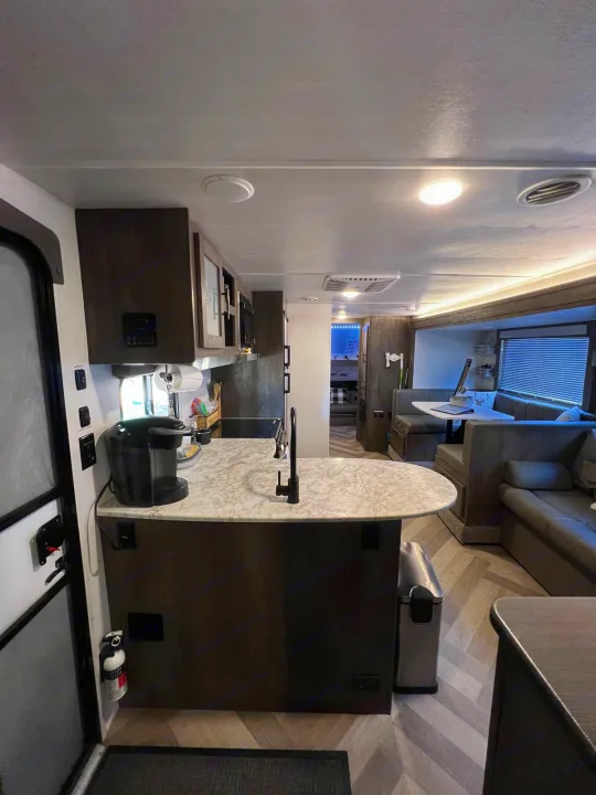 Spacious RV rental interior with modern kitchen, dining booths, and living area on herringbone flooring. Ready for adventures!. Forest River Wildwood X-Lite 2021
