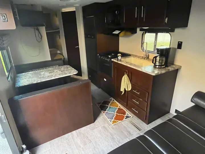 RV rental interior showcasing a compact kitchen with stove, sink, and coffee maker, dinette, and a black sofa bed.. Sportsmen LE 2018