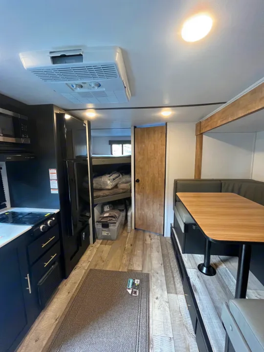 RV rental interior: full kitchen, dark cabinets, wood floors, dining dinette, and bunk bed area. AC unit on ceiling.. Keystone RV Springdale 2023