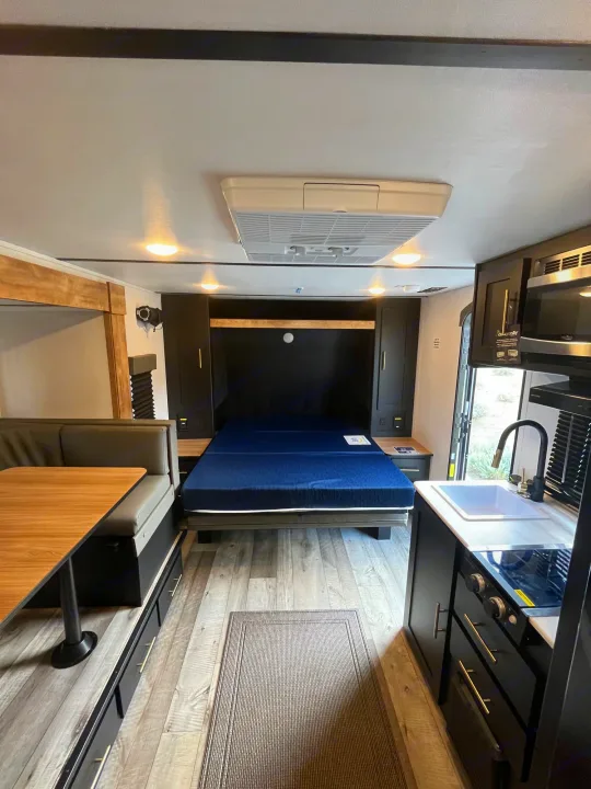 Modern RV rental interior showing a comfortable fold-down bed, dinette with storage, and a well-equipped kitchen area.. Keystone RV Springdale 2023