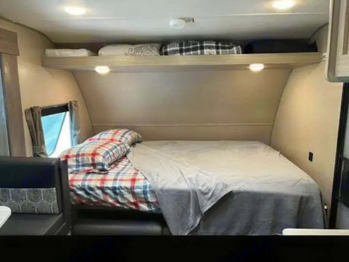 This RV rental offers a cozy bedroom with a comfortable bed, plaid bedding, overhead storage, and window, perfect for travel.. Coachmen Catalina Summit 184BHS 2022