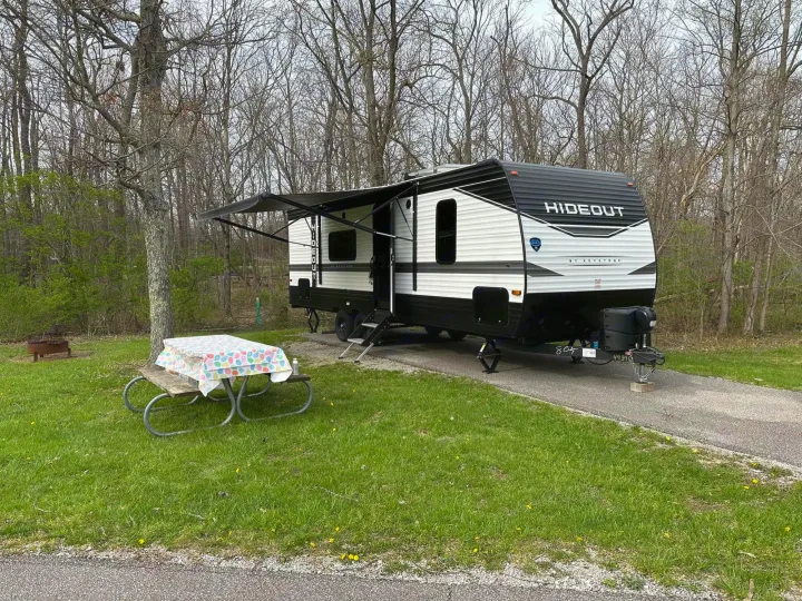 An RV rental travel trailer set up in a wooded campsite. Awning extended, picnic table ready for outdoor enjoyment.. Keystone RV Hideout 2022