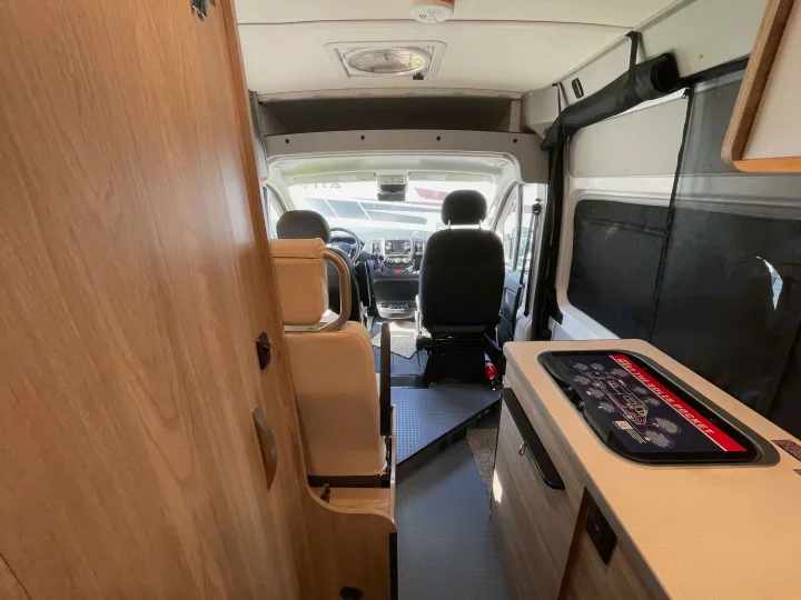 Compact Winnebago Solis Pocket RV rental interior. View from rear shows cockpit, small kitchen & wood cabinetry.. Winnebago Solis 2022