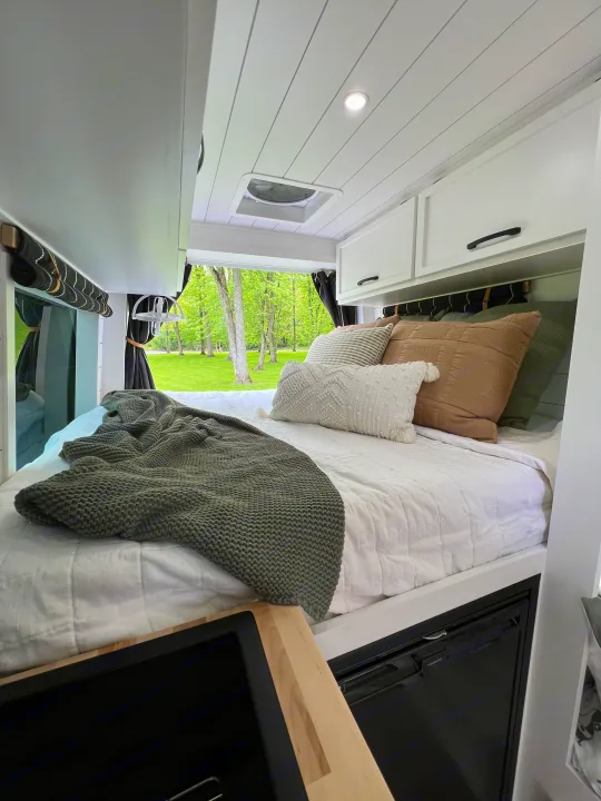 Cozy RV rental bedroom featuring a comfy bed with plush pillows, modern cabinets, and a beautiful nature view.. Mercedes-Benz Sprinter 2017