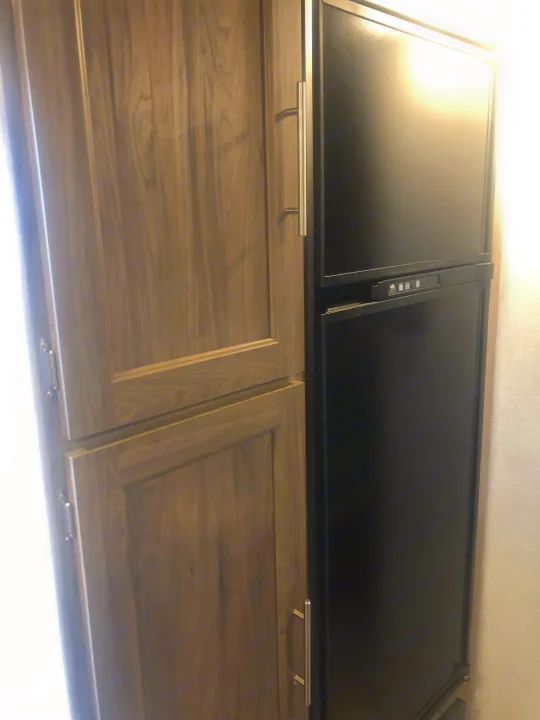 RV rental interior featuring a tall light wood cabinet beside a black two-door refrigerator with a control panel.. Crossroads RV Zinger Lite 2022