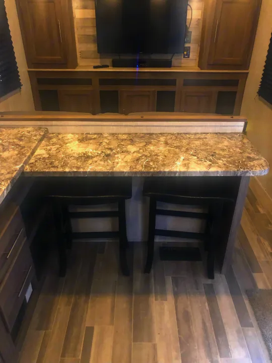 Explore this modern RV rental interior featuring a sleek kitchen bar with two stools and a built-in entertainment center.. Crossroads RV Zinger Lite 2022