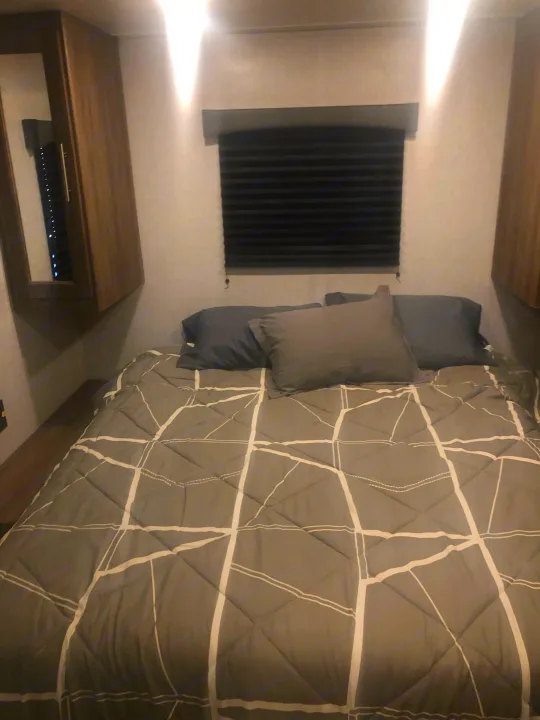 Cozy RV rental bedroom featuring a bed with gray geometric patterned bedding, window blinds, and wood cabinetry.. Crossroads RV Zinger Lite 2022