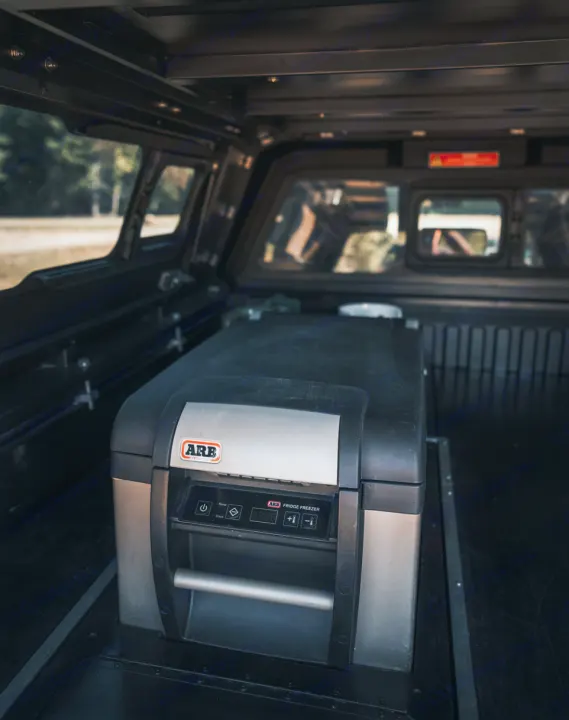 An ARB portable fridge freezer sits on a slide-out tray inside a vehicle's camper shell, great for rv rental.. Toyota Tacoma 2023