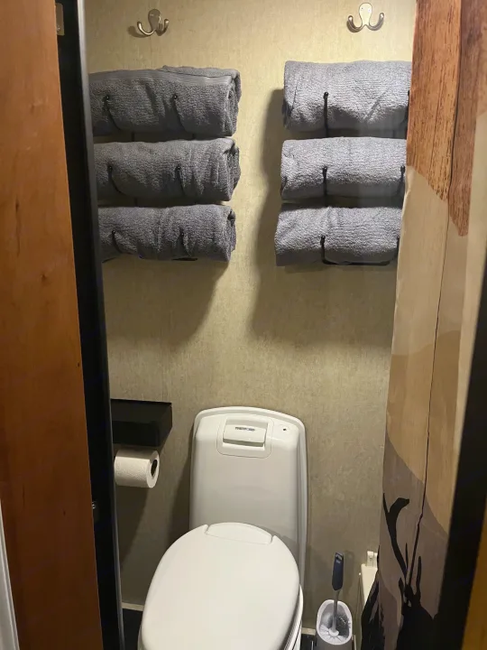 Compact RV rental bathroom with white toilet, gray rolled towels on wall racks, and essential amenities for your trip.. Forest River Cherokee Grey Wolf 2015