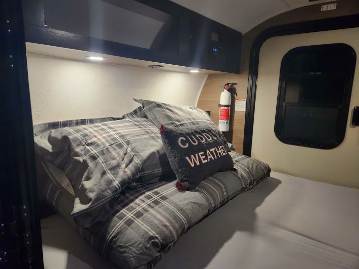 Cozy RV rental bedroom with plaid bedding, "Cuddle Weather" pillow, and essential fire extinguisher.. Braxton Creek Bushwacker 2023