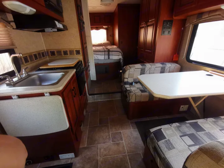 RV rental interior. View of kitchen area with sink & stove, dinette, and a peek into the bedroom.. Forest River Sunseeker 2010