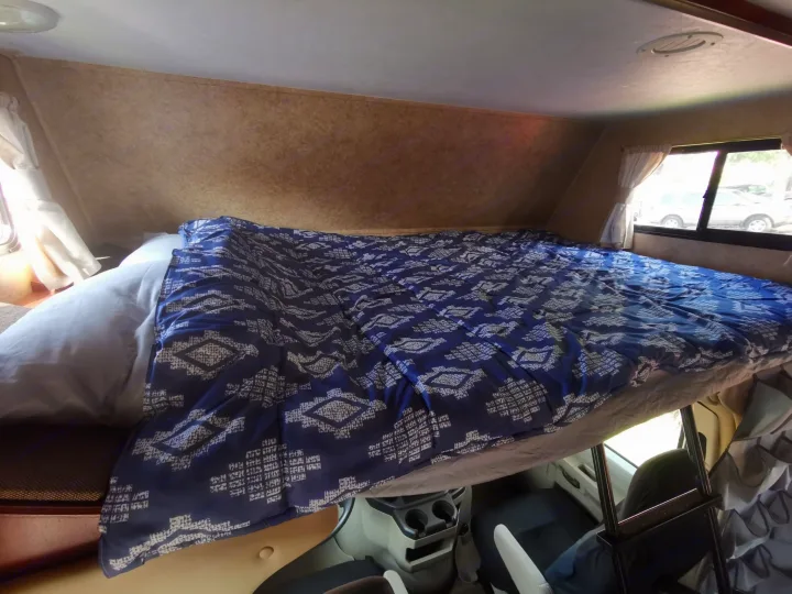 Inside an RV rental: a comfortable over-cab bunk bed with a blue patterned comforter, offering a cozy sleep space.. Forest River Sunseeker 2010