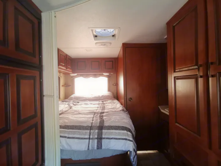 Cozy RV rental bedroom featuring a striped bed, wood cabinets, and bright natural light, ideal for your next adventure.. Forest River Sunseeker 2010