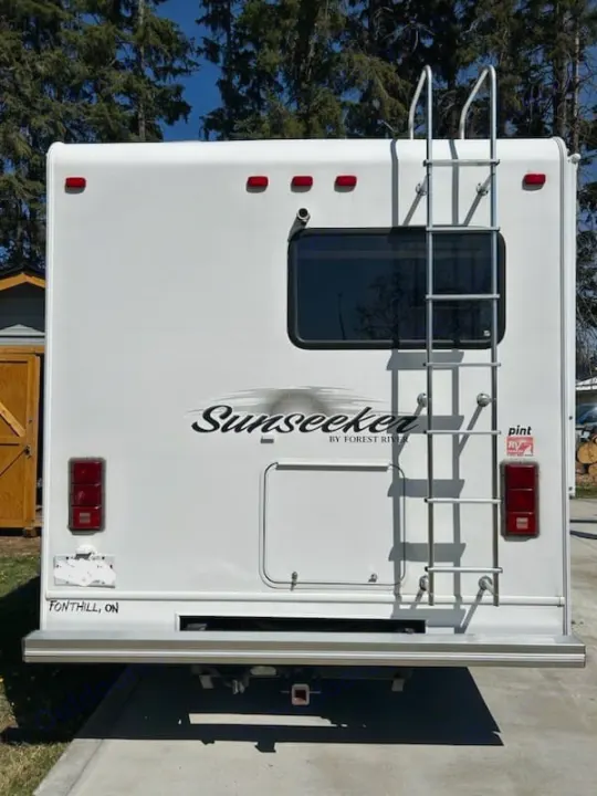 Rear of a white Sunseeker RV rental, featuring a ladder, window, and tail lights.. Forest River Sunseeker 2010
