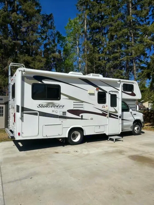 White Sunseeker RV rental parked on a sunny concrete pad with tall trees in the background. Ready for adventure.. Forest River Sunseeker 2010