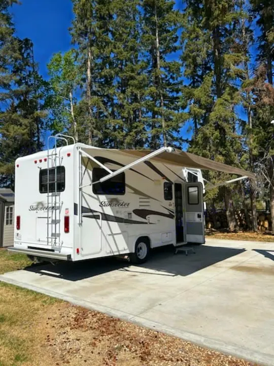 White Sunseeker RV rental parked on concrete with awning extended under blue sky and tall trees. Ready for adventure!. Forest River Sunseeker 2010